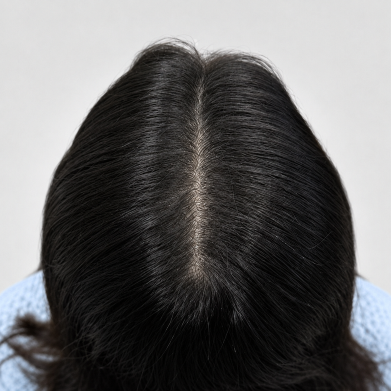 Top view of dark hair with a center part showing natural-looking density enhancement with scalp micropigmentation